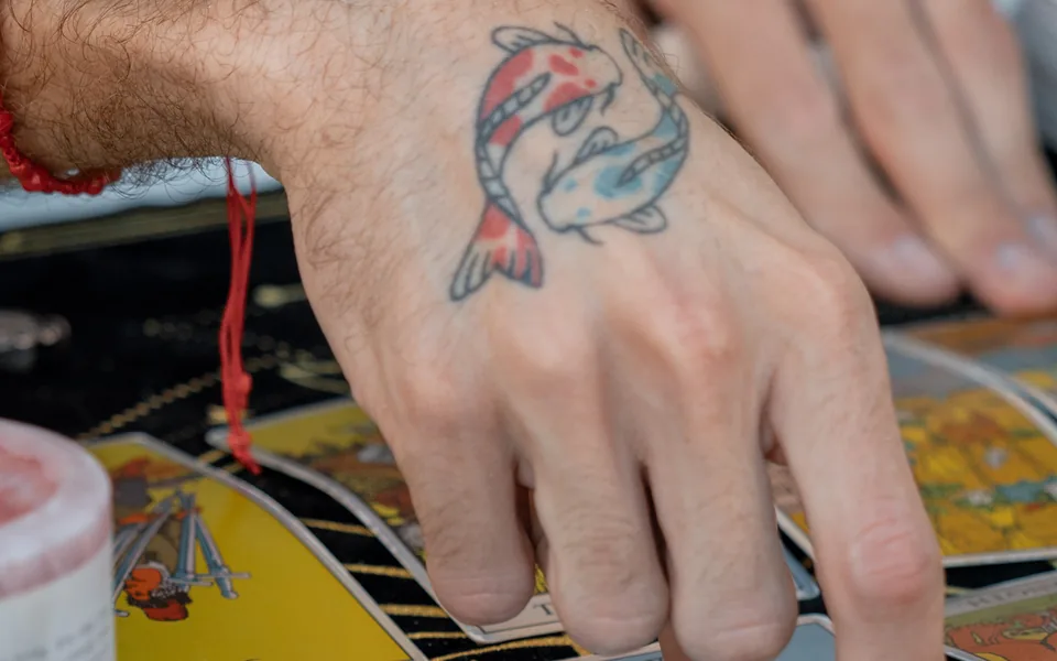 Alex's tattooed hand resting on a tarot spread mid-reading